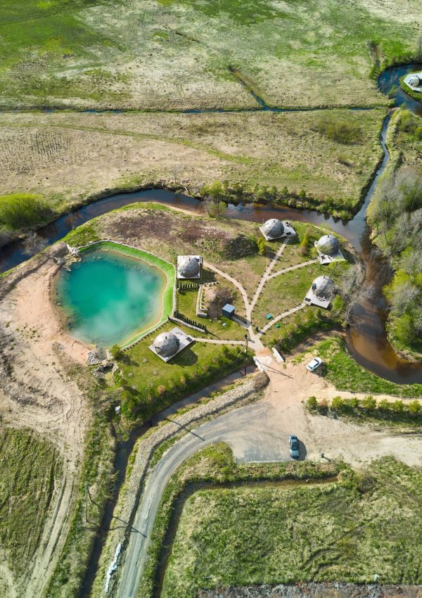 Experience a stunning aerial view of a rustic retreat with charming cabins and a peaceful healing pond